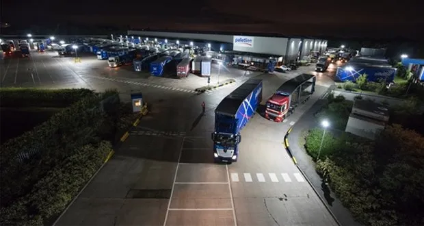 Busy Palletline distribution hub at night with multiple lorries loading and unloading under floodlights.