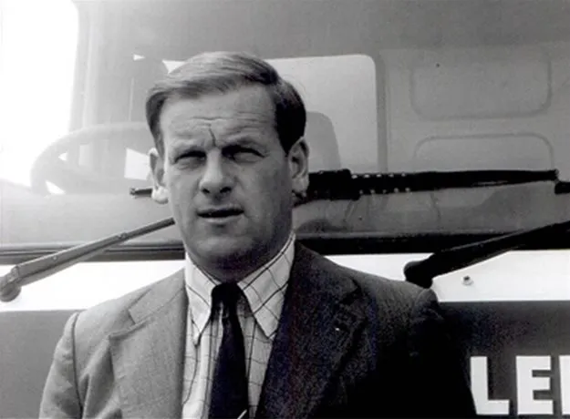 Black and white portrait of a man in a suit and tie standing in front of a lorry cab