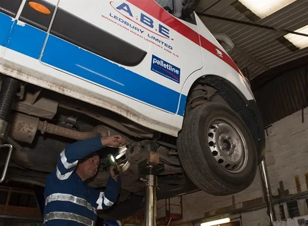 Mechanic working underneath an ABE Ledbury Limited van raised on a hydraulic lift inside a garage