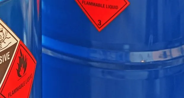 Close-up of blue industrial drums with red hazard labels for flammable liquid and explosive materials.